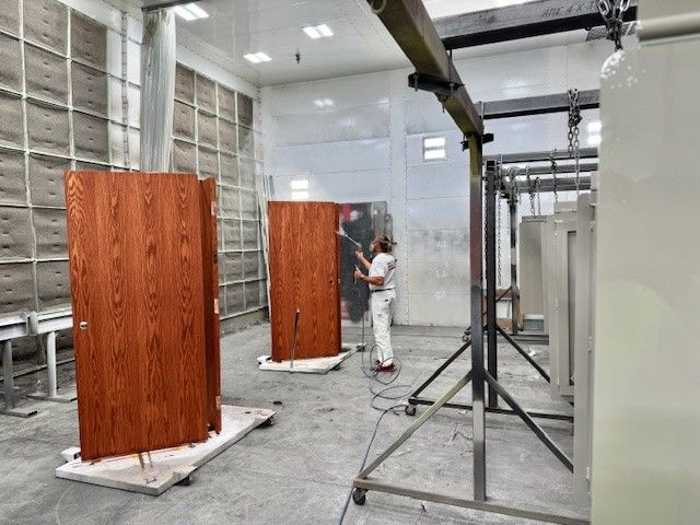 Worker spray-painting a tall wooden panel in an industrial workshop