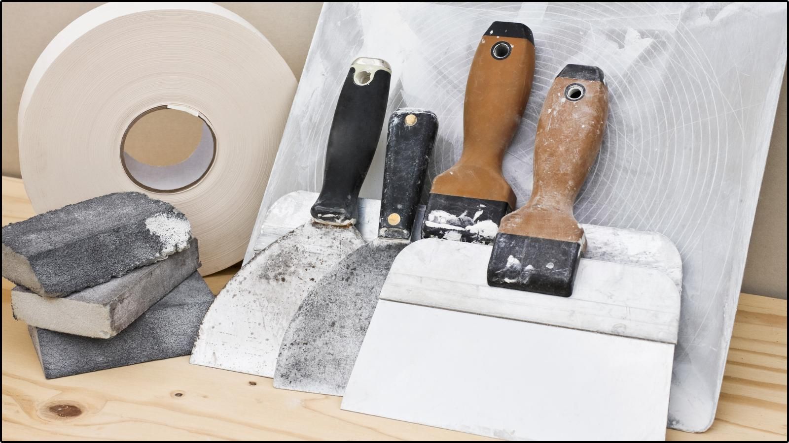 drywall patch A spatula is sitting on a wooden table next to a roll of tape