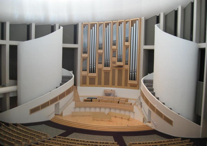 Concert hall stage with organ pipes, curved white panels, and empty audience seating
