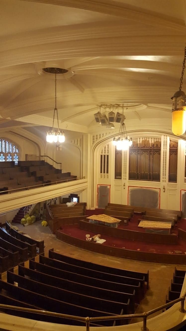 Empty ornate theater interior with curved balcony seating, stage, and warm hanging lights