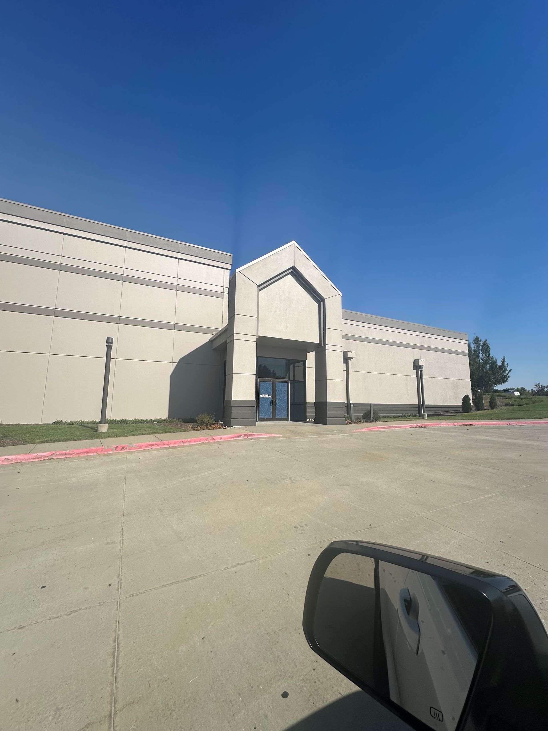 Large beige building with a central entrance under a clear blue sky, viewed from a parking lot.