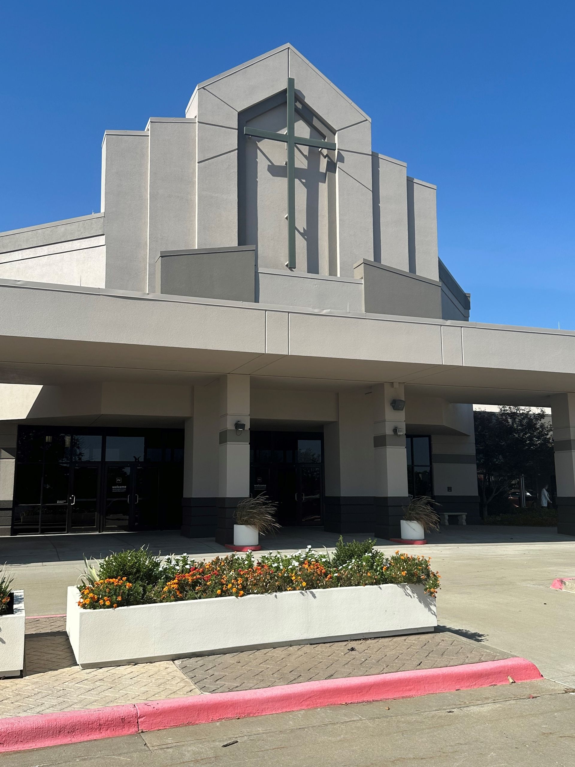 Modern building entrance with a covered drive-through, concrete facade, and flower planter at curbside