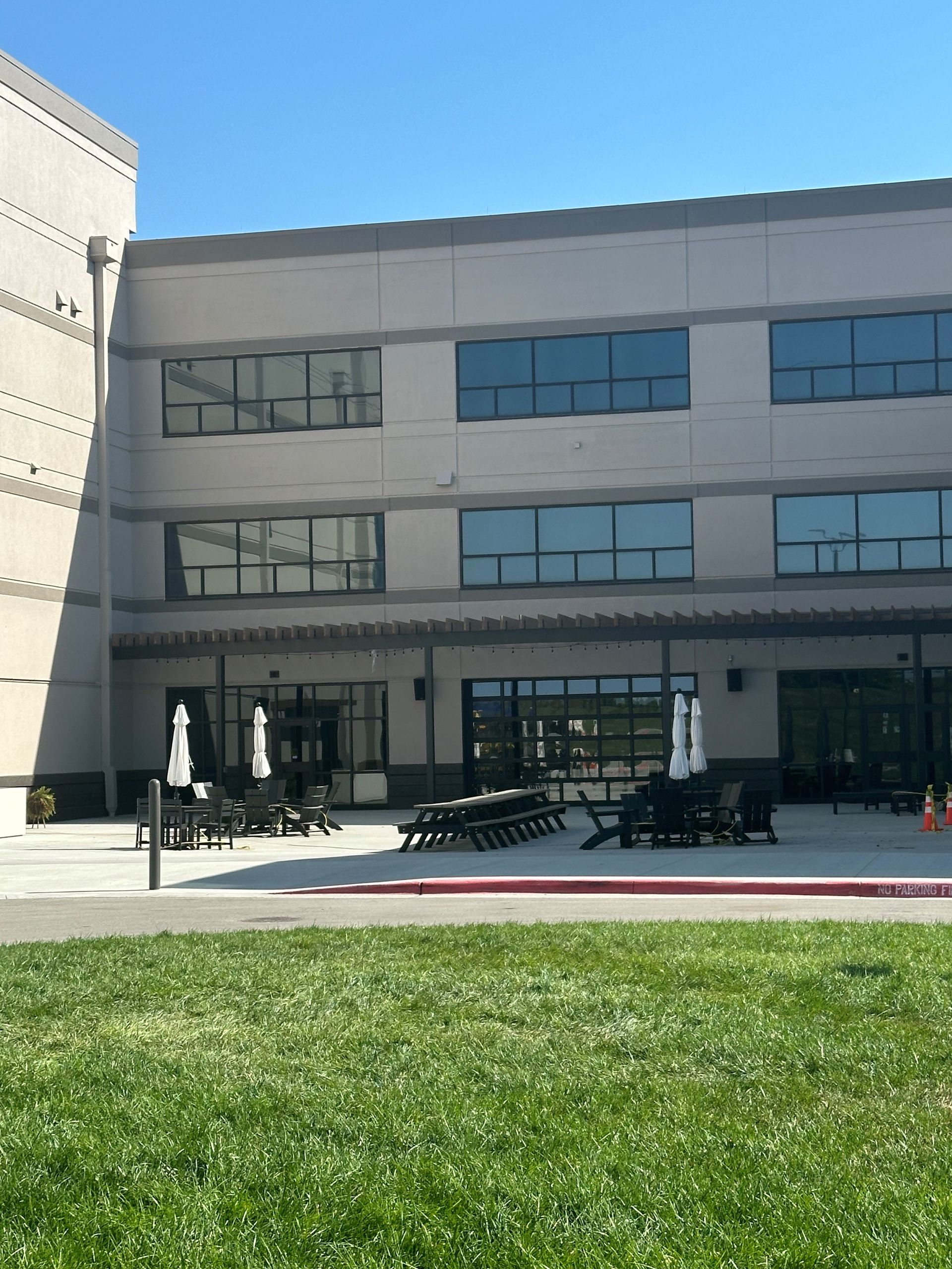 Modern building exterior with a green lawn, windows, and a shaded entrance area