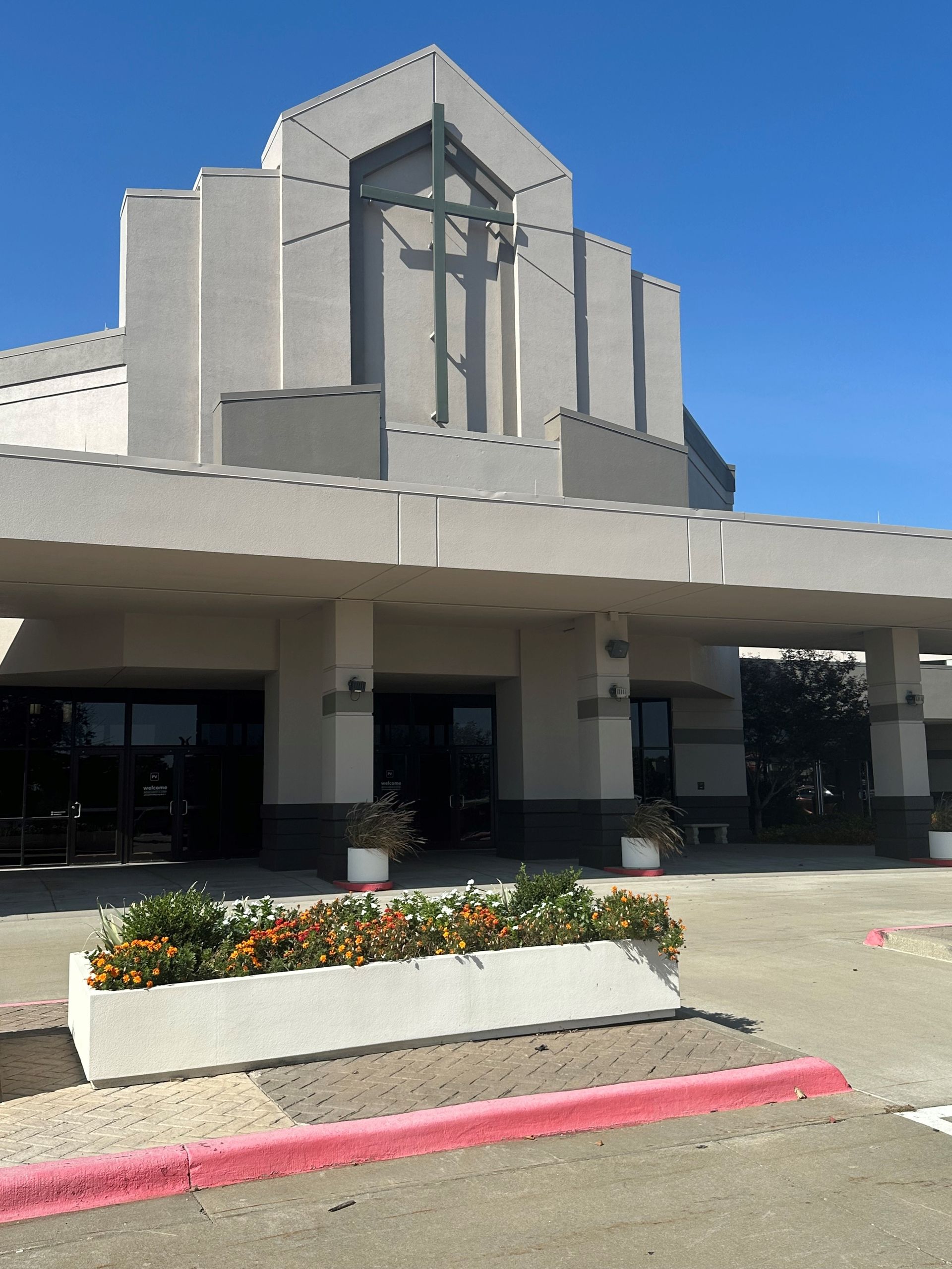 Building entrance with white facade, covered walkway, and flower planter by the curb