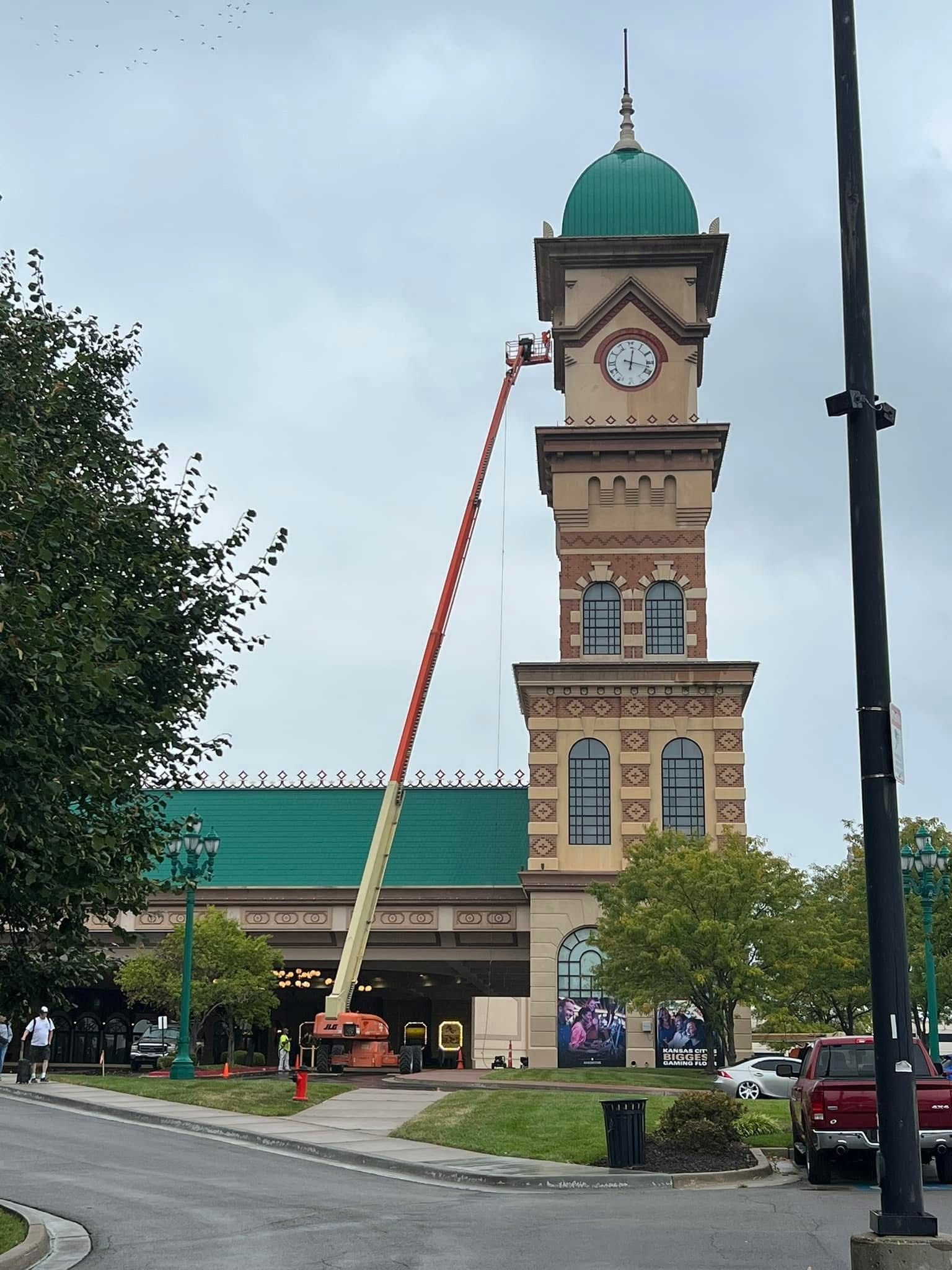 Historic clock tower with green dome and crane beside it on a cloudy street scene