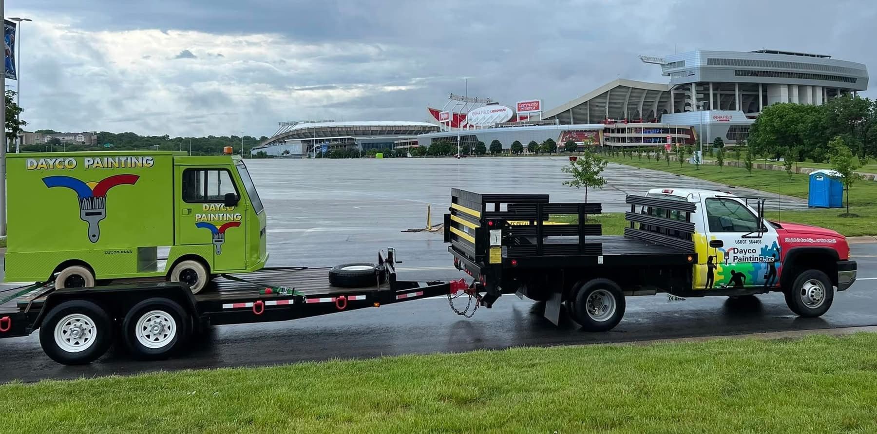 Two colorful tow trucks parked on a wet apron near an airport terminal, with an airplane in the background.