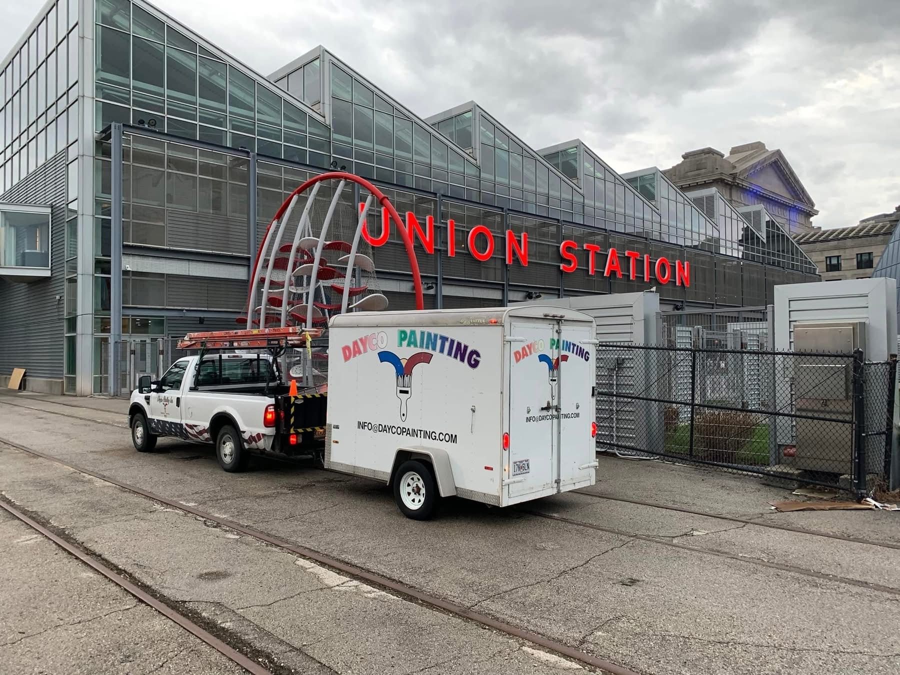 White truck and trailer parked outside Union Station, with glass train hall and red station sign.