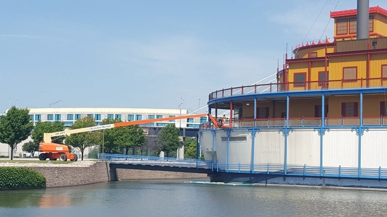 Waterfront industrial building with blue trim beside a canal, with an orange truck in the distance.