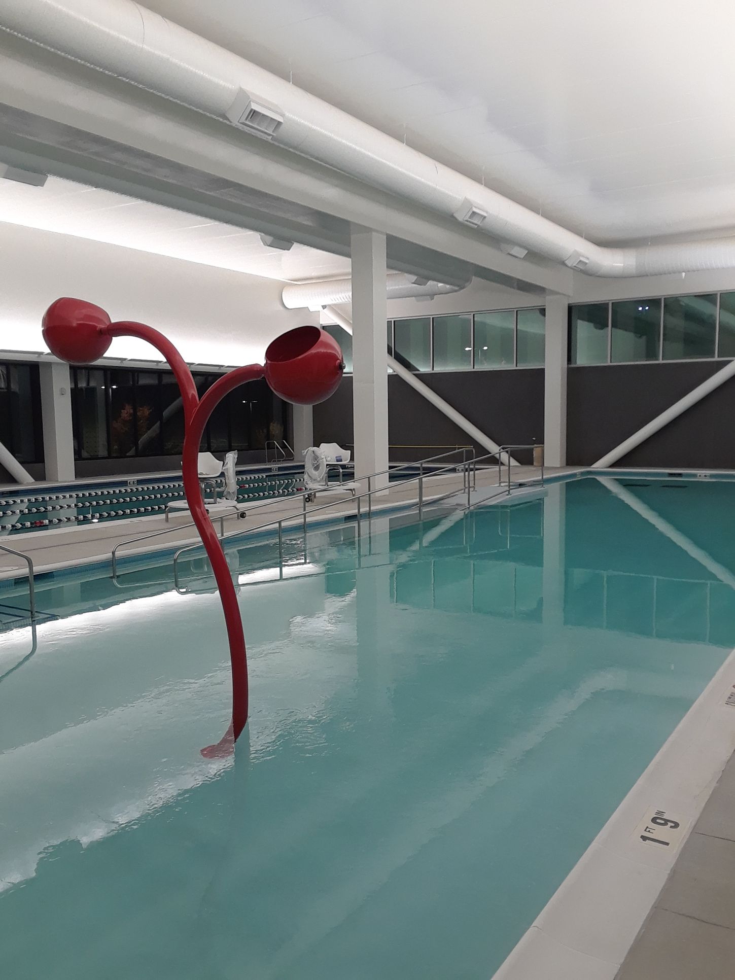 Indoor pool with pale blue water and red bubble fountain under white beams and glass walls