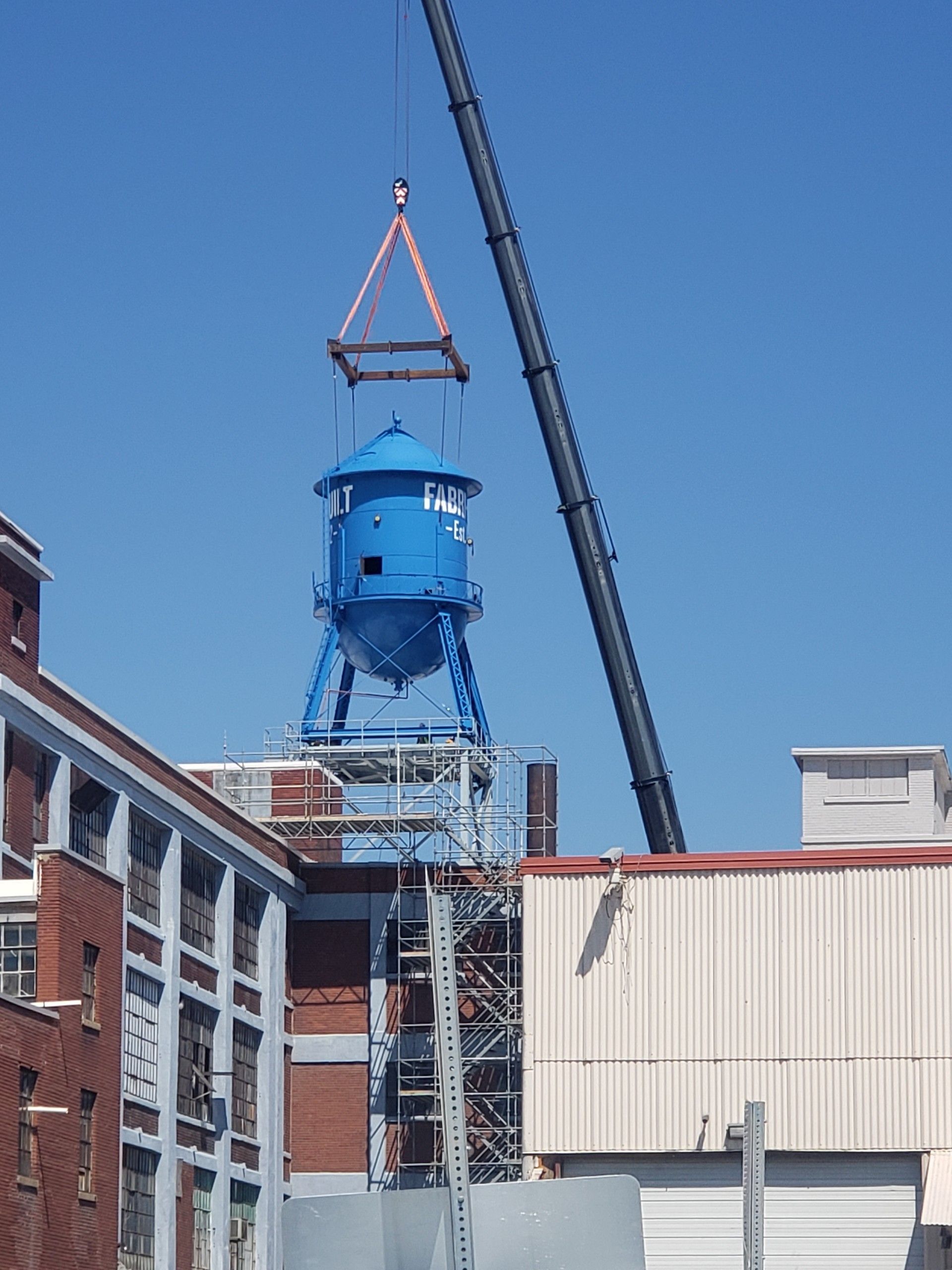 Blue industrial tower being lifted by a crane above buildings at a construction site