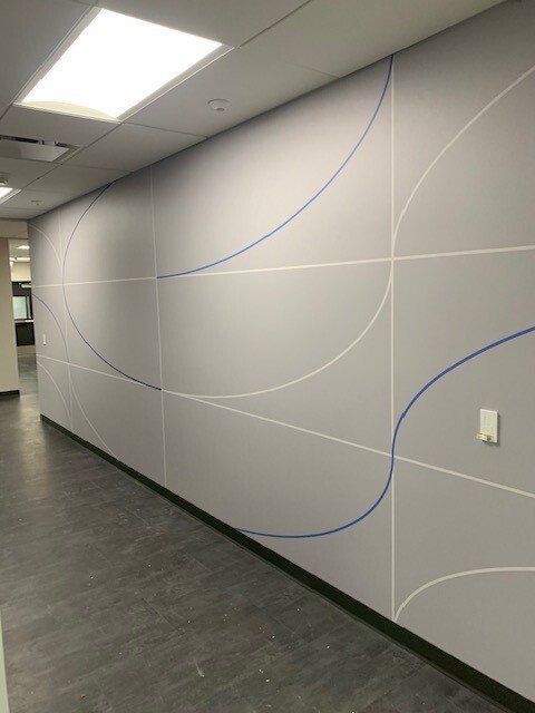 Curved gray hallway wall with blue and white accent lines under fluorescent ceiling lights