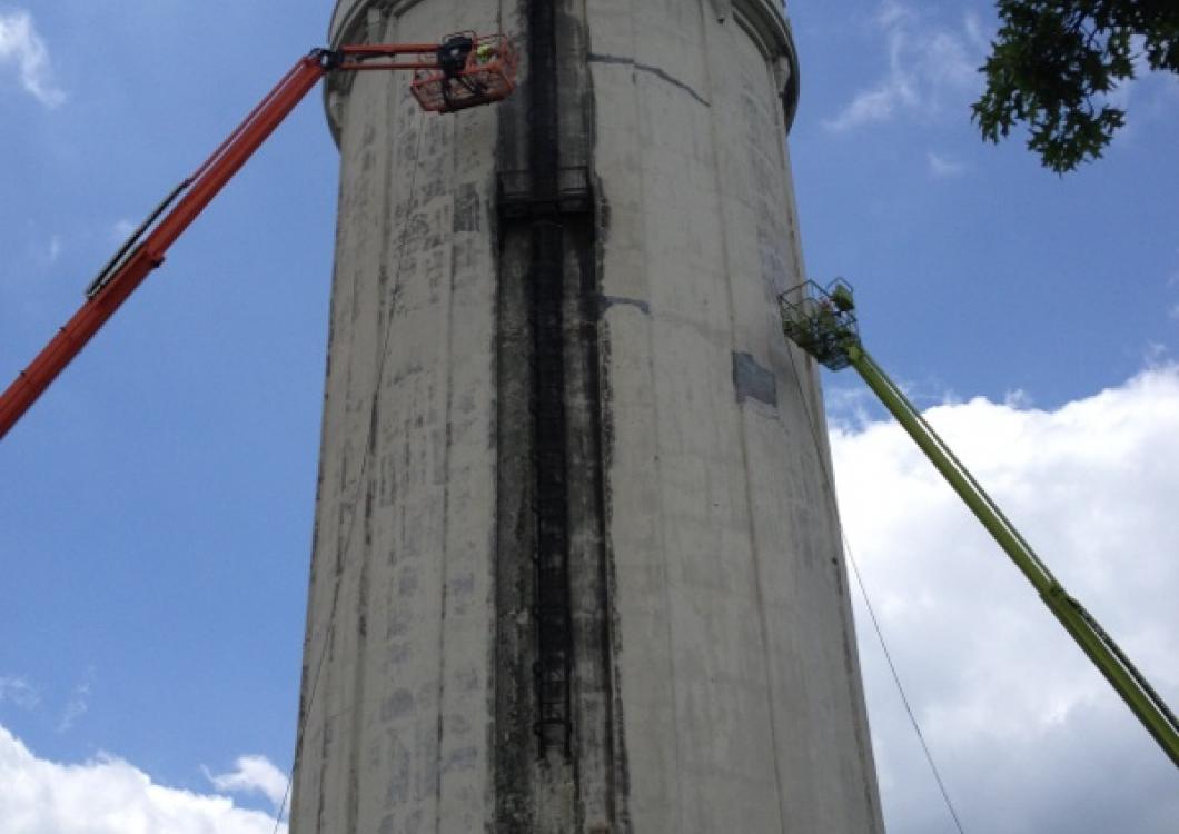 Two boom lifts with workers inspecting a tall concrete tower against a blue sky