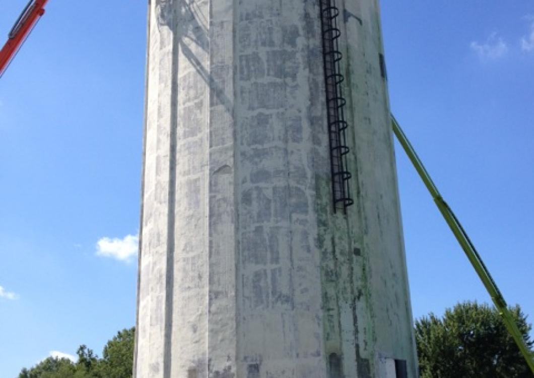 Tall concrete tower against blue sky, with construction cranes and a ladder on one side.