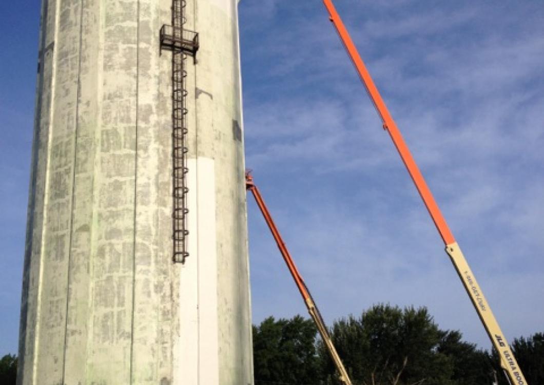 Tall white tower with ladder and two orange crane booms against a blue sky