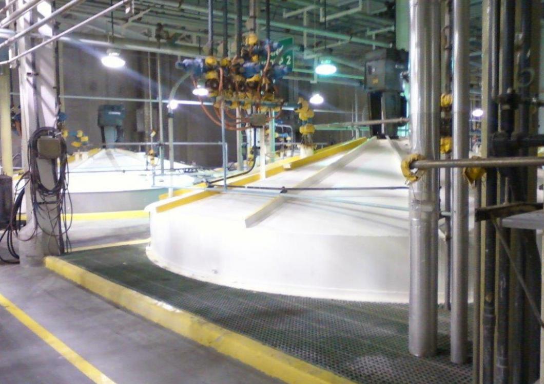 Large industrial facility with white storage tanks and overhead machinery inside a factory hall