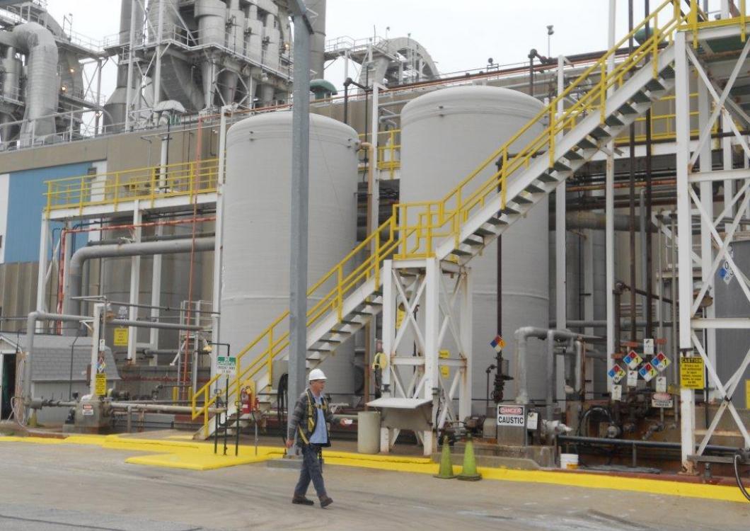 Industrial plant with silver tanks, yellow stairways, and a worker walking in the foreground