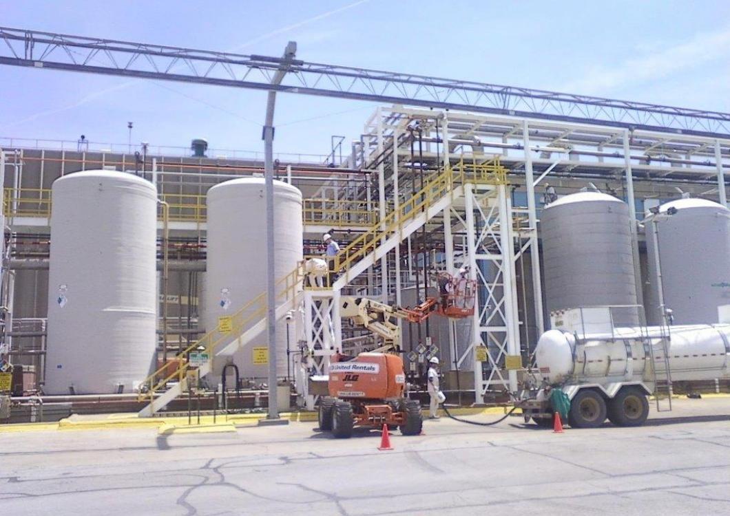 Industrial plant with silver tanks, piping, and orange lift on a concrete worksite.
