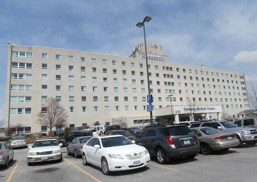 Large beige building with many windows, a parking lot full of cars, and a blue sky overhead