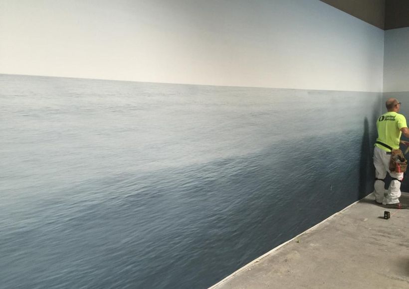 Two workers painting a wall mural of an ocean horizon along a hallway.