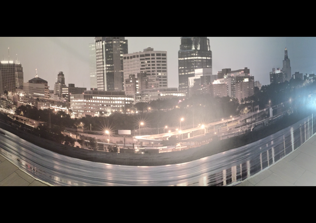 Nighttime city skyline with illuminated buildings and a curved glass structure in the foreground