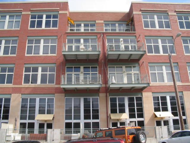 Red brick apartment building with balconies and large windows above parked vehicles.