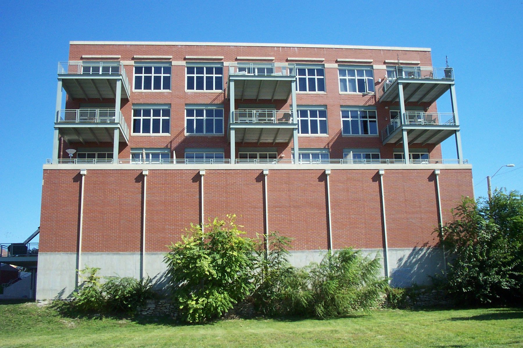Brick apartment building with balconies and large windows above a grassy lawn and shrubs