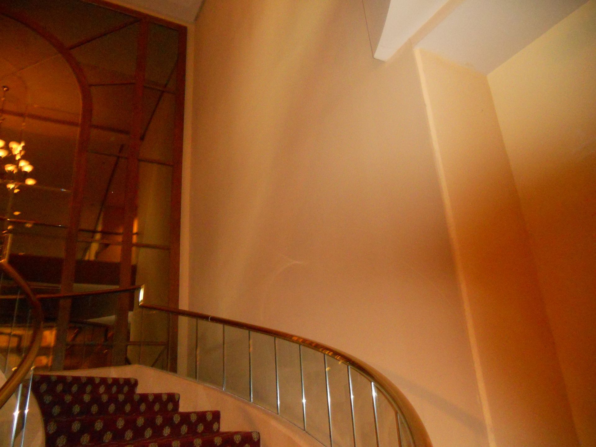 Curved staircase with glass railing in a warmly lit interior lobby.