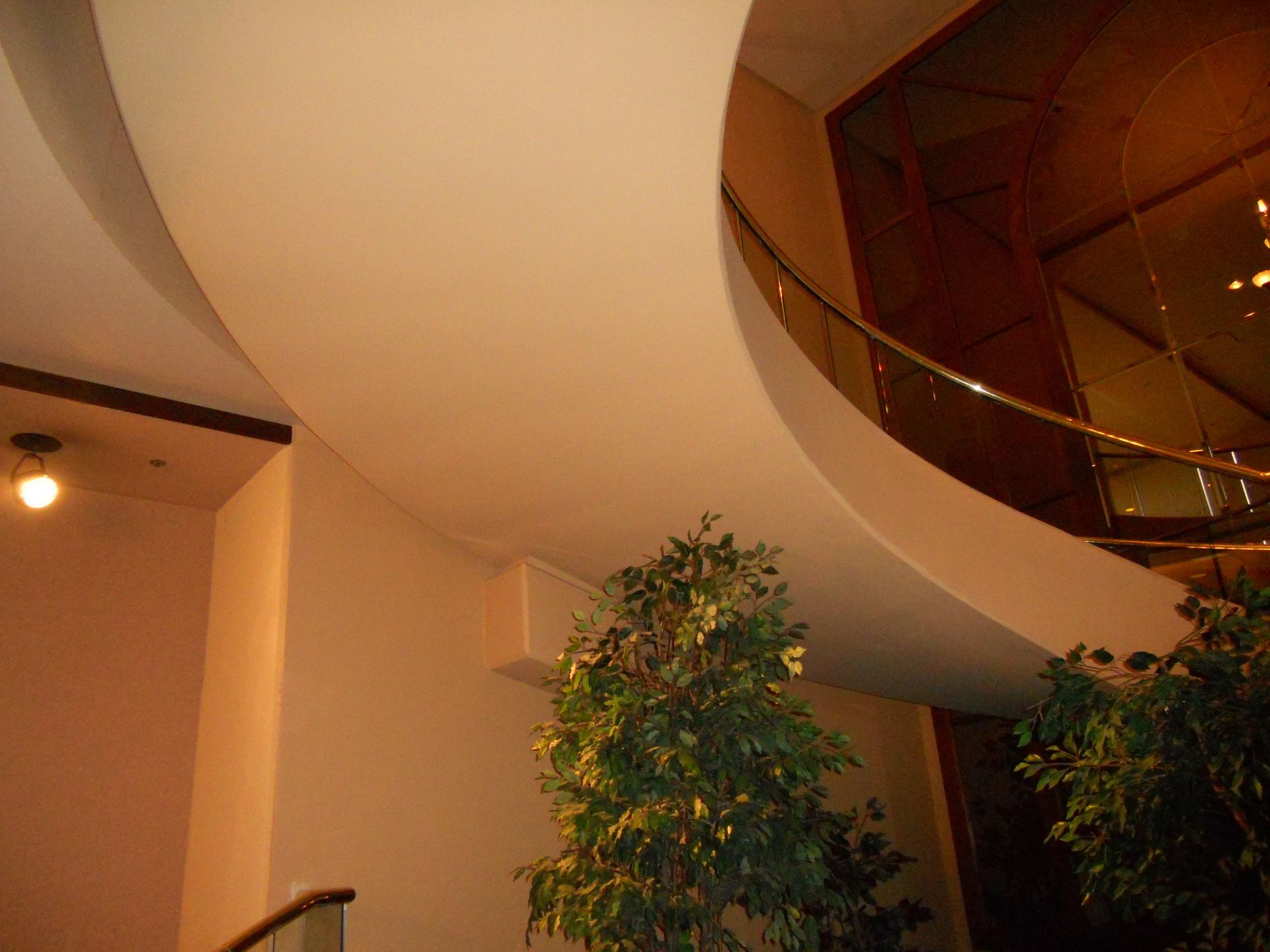 Curved indoor ceiling with warm lights, a potted plant, and a glass-railed balcony