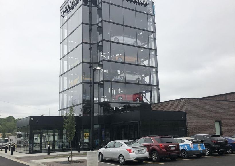 Tall glass tower beside a parking lot with several cars under a cloudy sky