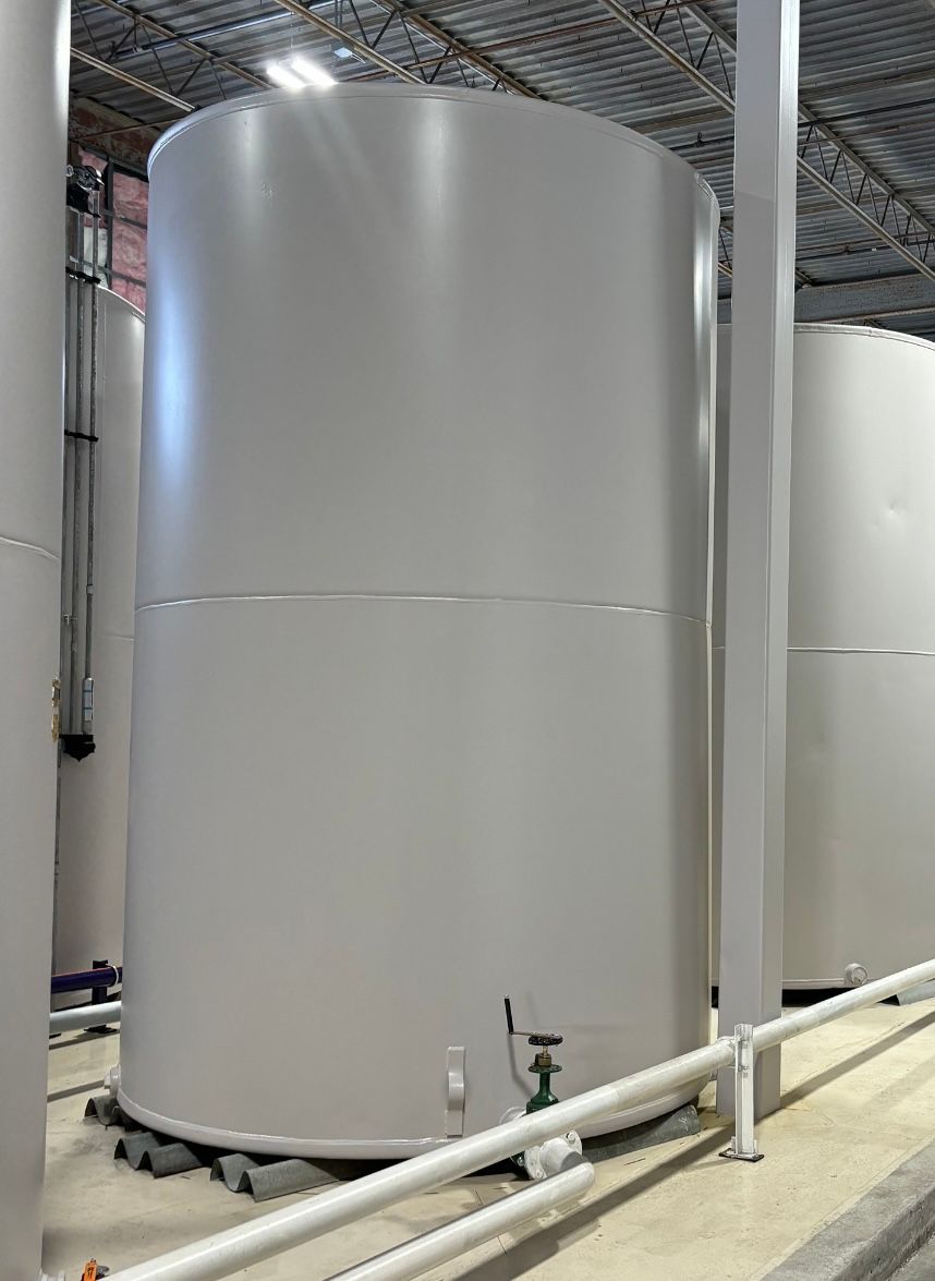 Large white cylindrical storage tanks in an industrial facility, with pipes and a metal roof overhead