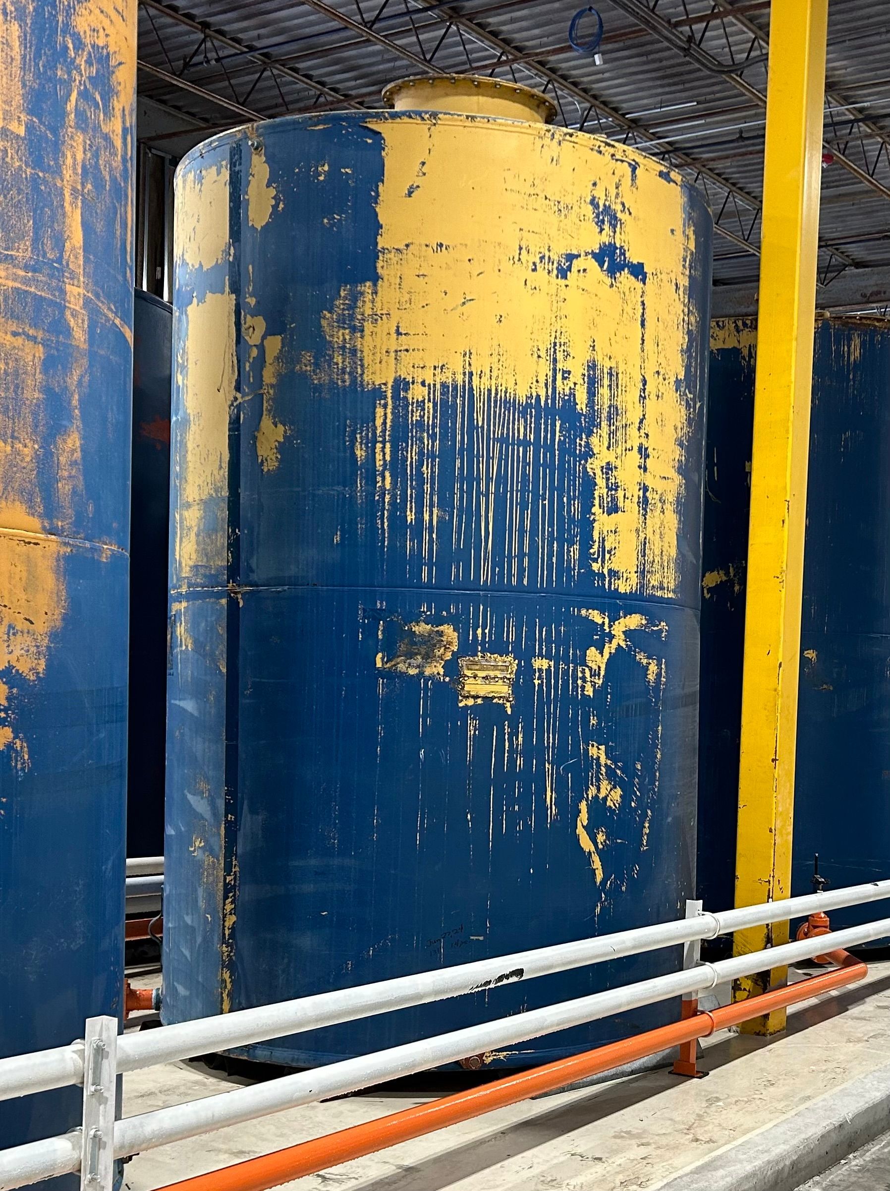 Blue and yellow painted concrete structure beside a railing, with chipped paint and construction surroundings