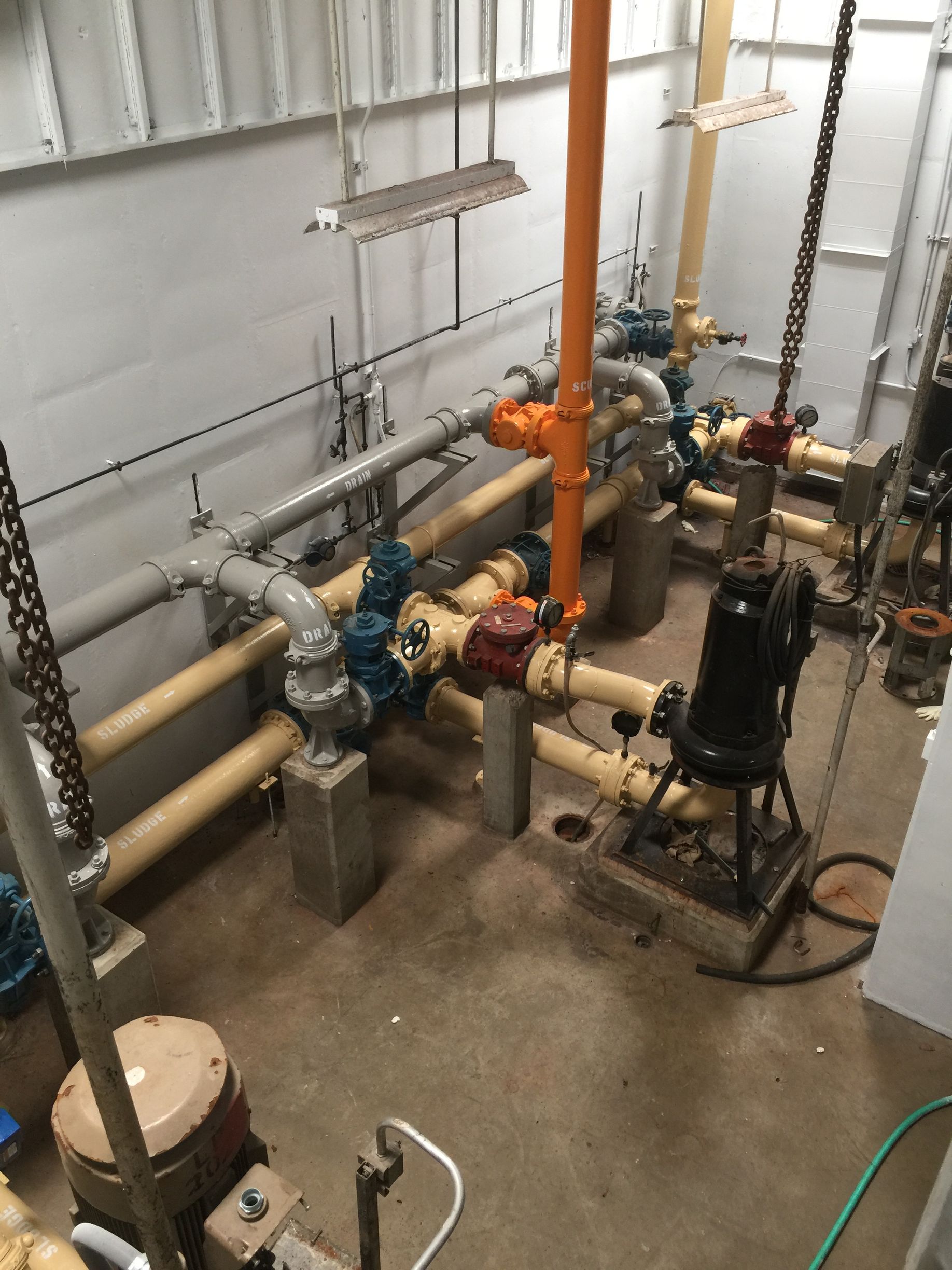 Industrial mechanical room with pipes, valves, pumps, and tanks on a concrete floor