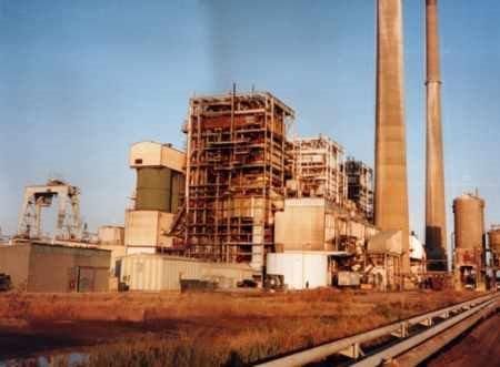 Industrial power plant with tall smokestacks and scaffolding under a clear blue sky