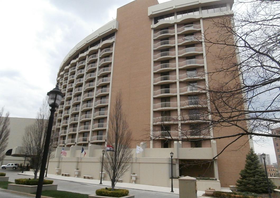 Tall apartment building with curved balconies beside leafless trees on an overcast day