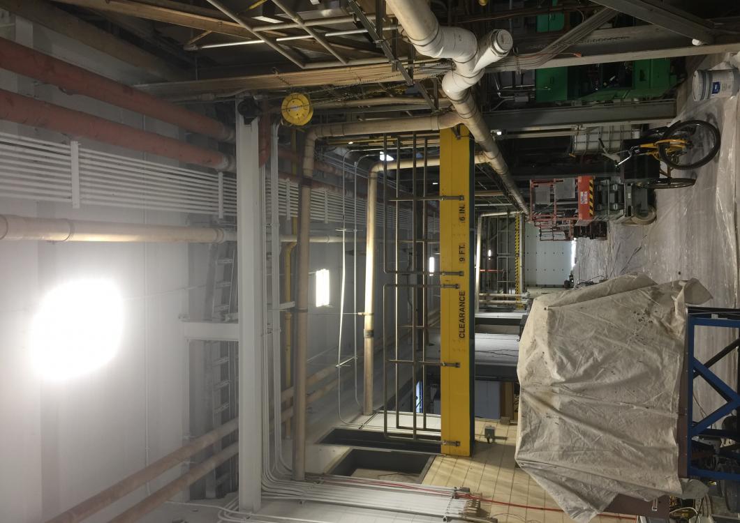Industrial construction site with exposed pipes, steel framing, and covered equipment indoors