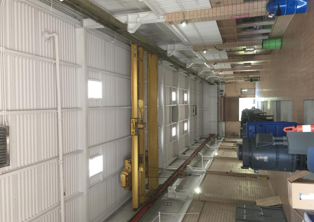 Industrial corridor with metal walls, pipes, windows, and blue machinery in a utility room