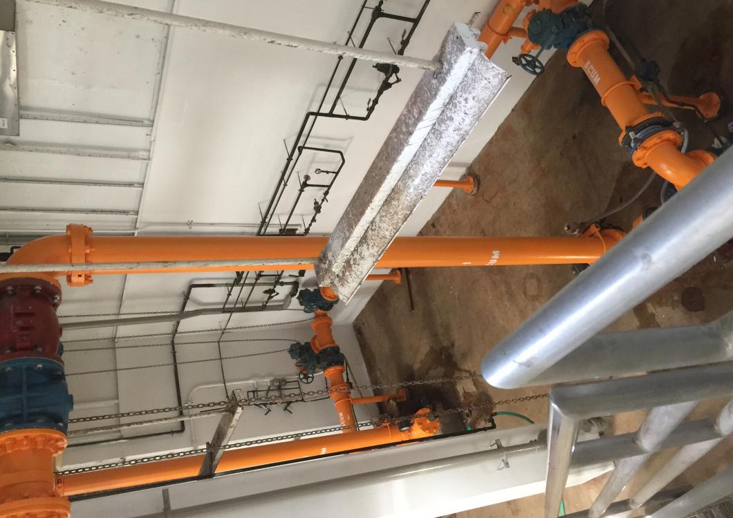 Orange industrial pipes and ducts running across a ceiling in a utility room