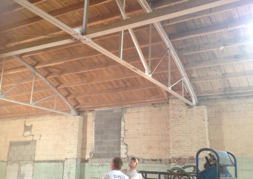 Warehouse interior with wooden roof trusses and two people standing below a brick wall