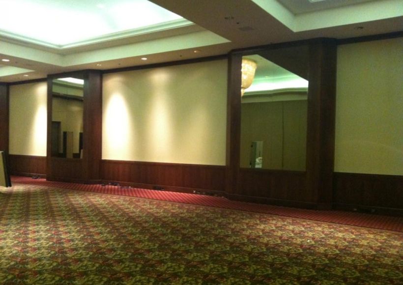 Empty carpeted hotel hallway with mirrored columns and wood-paneled walls