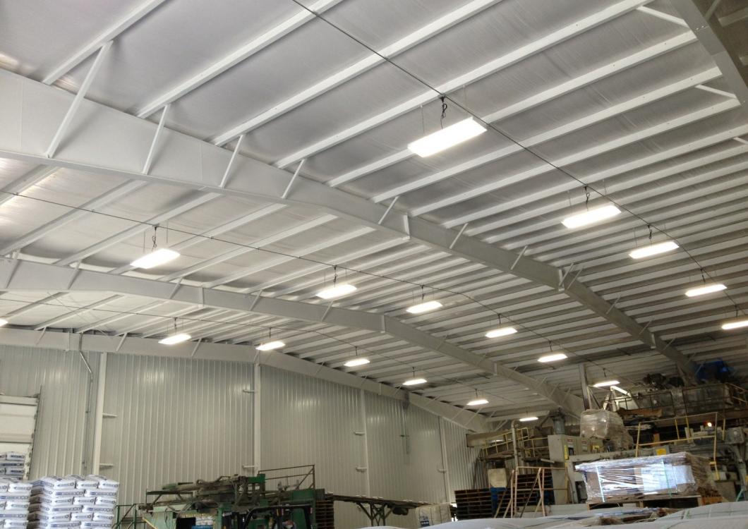 Interior of a large warehouse with white ceiling beams, hanging lights, and stacks of goods below