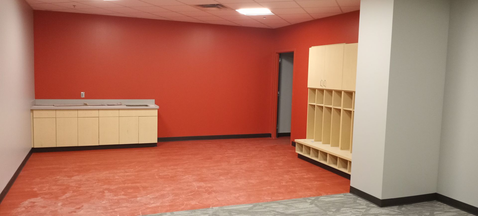 Empty room with red walls, tiled floor, cabinets, and built-in wooden cubbies.