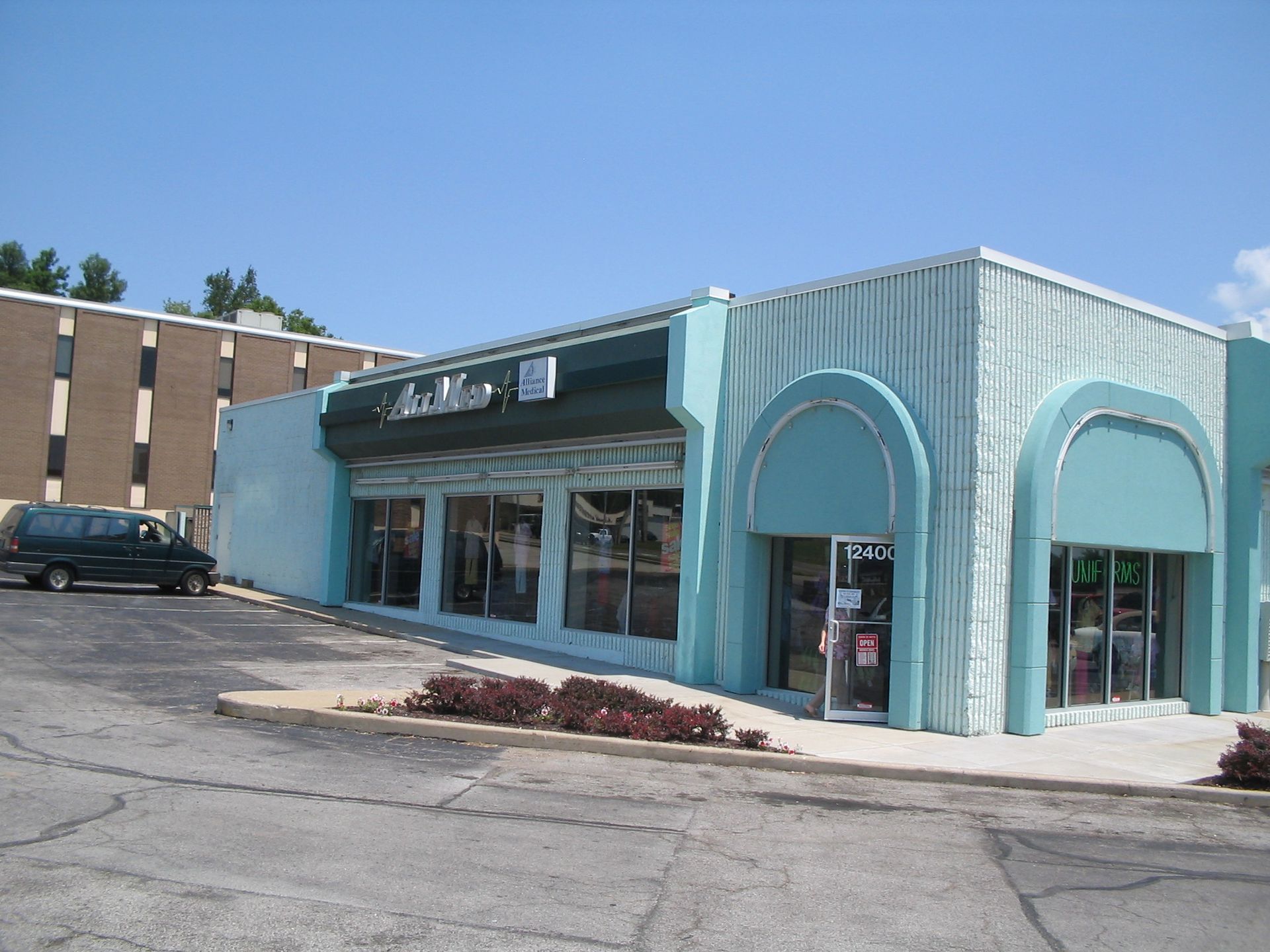 Turquoise storefront on a street corner with arched windows and a parked car nearby