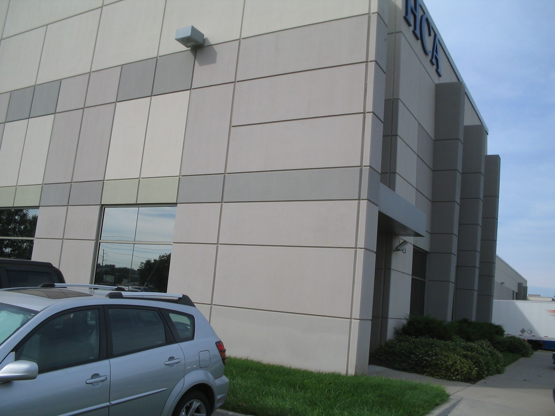 Parking lot beside a modern beige office building with a silver car in the foreground.