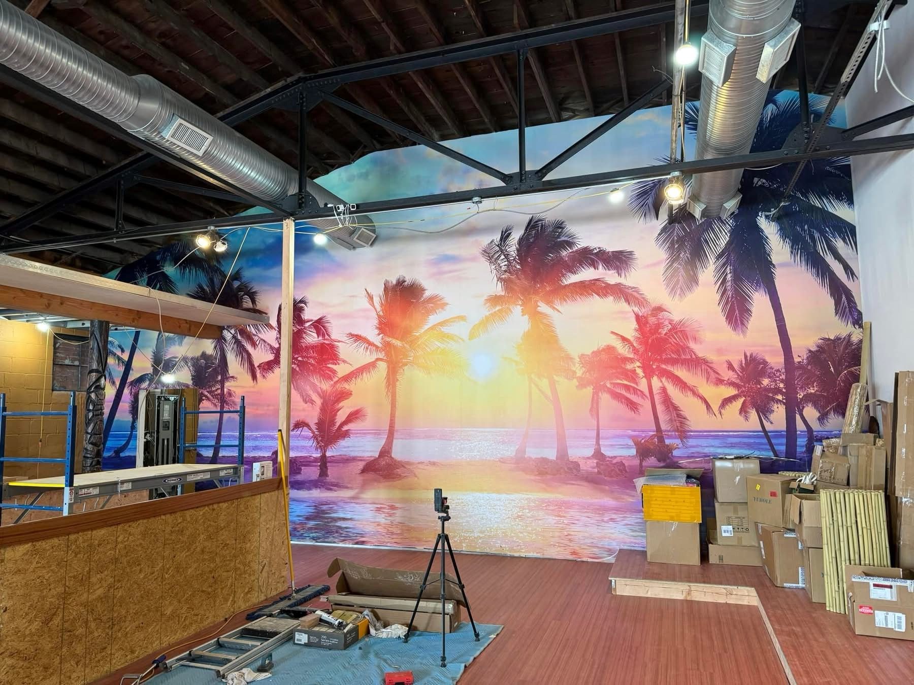 Indoor space with a large tropical sunset mural, bar counter, and camera tripod in the foreground