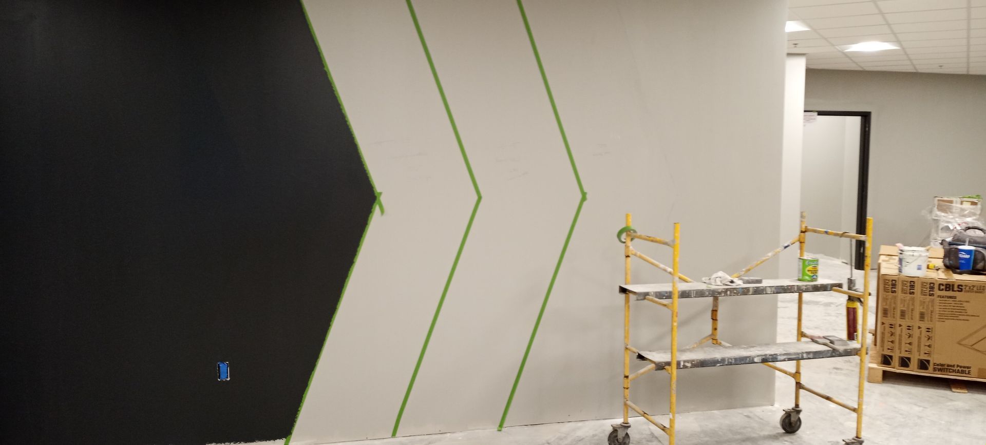 Construction area with green chevron wall design, scaffolding, and materials in a hallway.