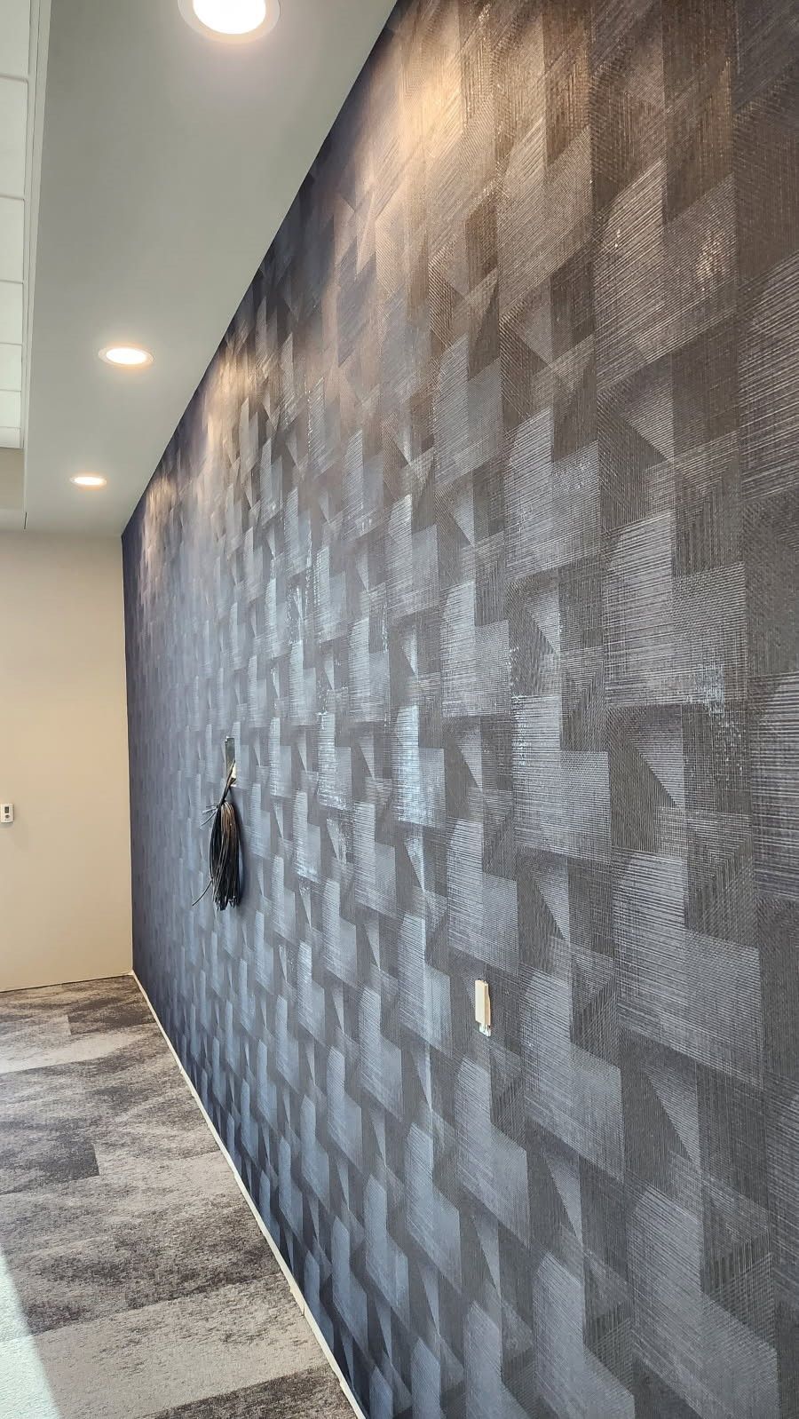 Modern hallway with gray patterned wall, recessed ceiling lights, and marble floor.