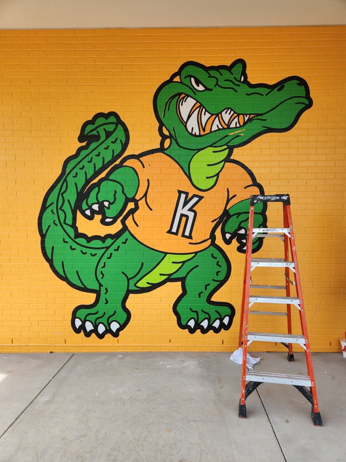 Green alligator mascot mural on yellow wall with a ladder in front