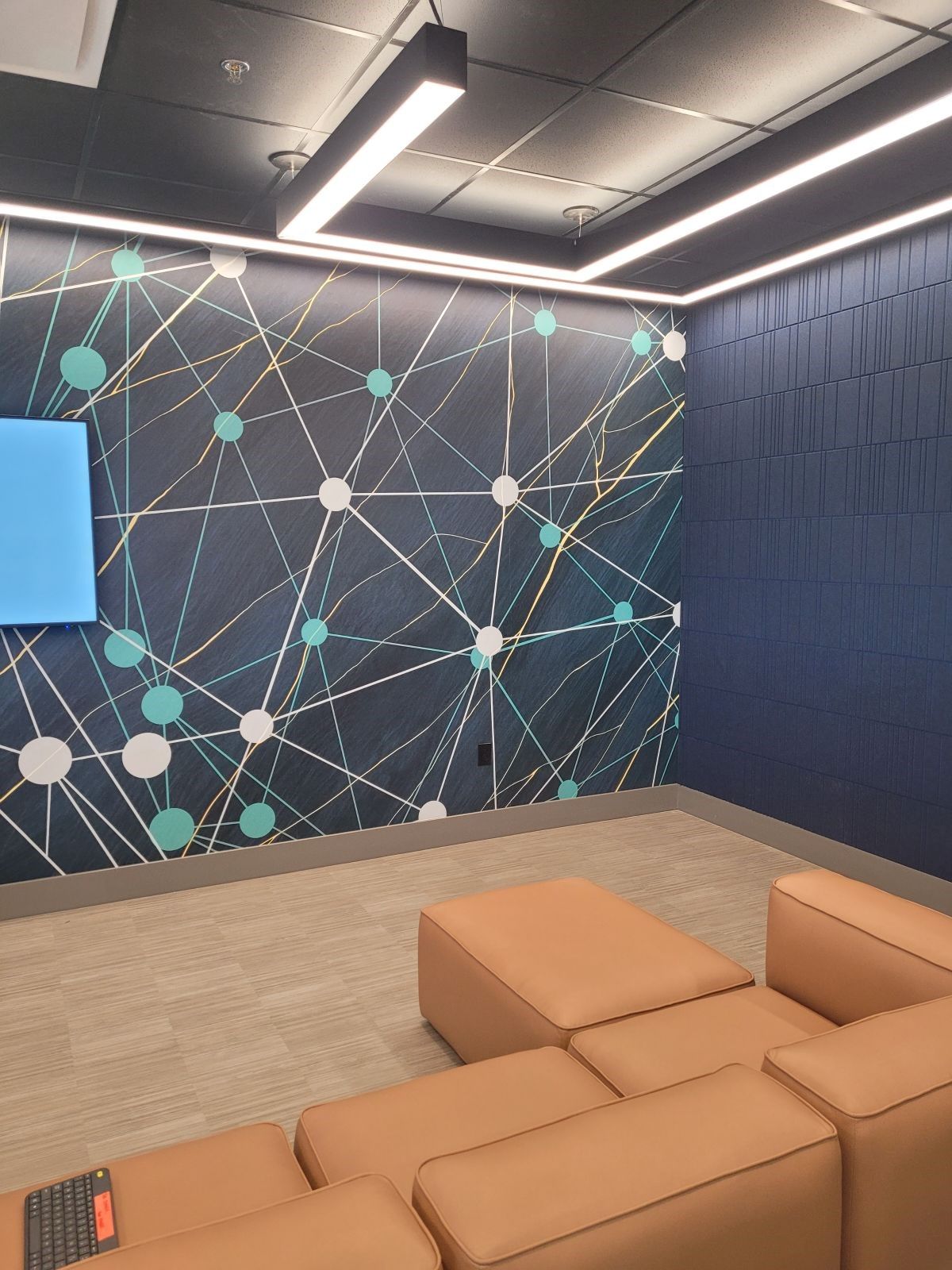Modern office lounge with tan couches, patterned accent wall, and ceiling lights