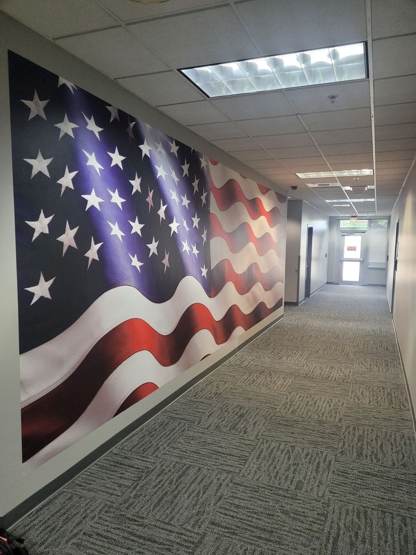 Long hallway with a large American flag mural on the left wall and carpeted floor