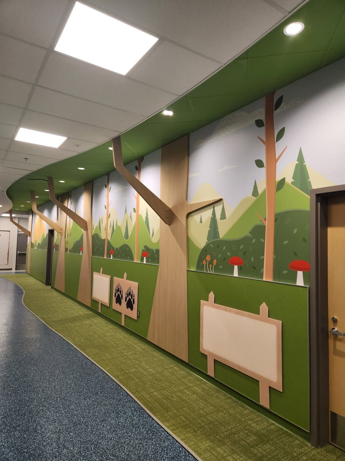 Hallway with a whimsical forest mural and blank wooden signboards along a green wall
